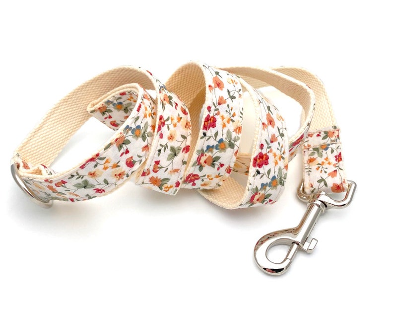 May include: A white cotton dog leash with a floral print featuring red, orange, and yellow flowers. The leash has a silver metal clip.