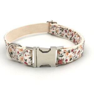 May include: A white dog collar with a floral pattern featuring small red, orange, and yellow flowers. The collar has a silver buckle and a silver D-ring.