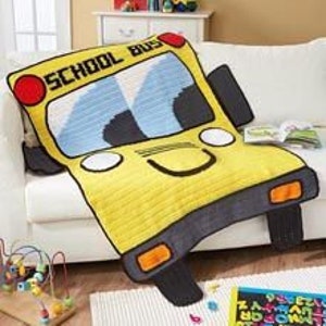 以下が含まれることがあります： 笑顔の顔、黒い車輪、側面に「SCHOOL BUS」と書かれた、黄色い学校バスの形をした、かぎ針編みの毛布です。