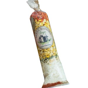 May include: A clear plastic bag filled with ingredients for corn chowder soup. The bag has a label that says "Santa Barbara Soups" and "Corn Chowder".