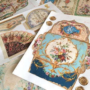 May include: A set of vintage paper ephemera featuring intricate floral designs, gold accents, and a blue and gold patterned box. The paper pieces are printed on a white background and have a distressed, antique look.
