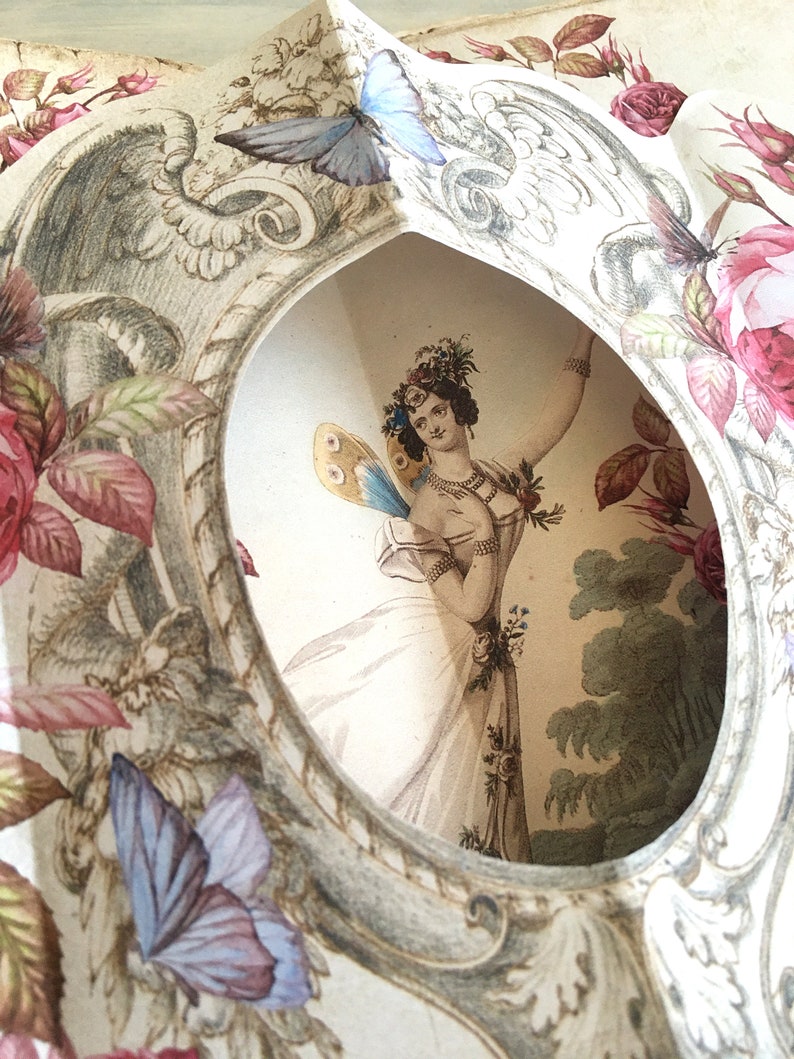May include: A vintage paper cut-out with a delicate floral design. A woman with a floral crown and butterfly wings is depicted in the center, surrounded by roses and butterflies.