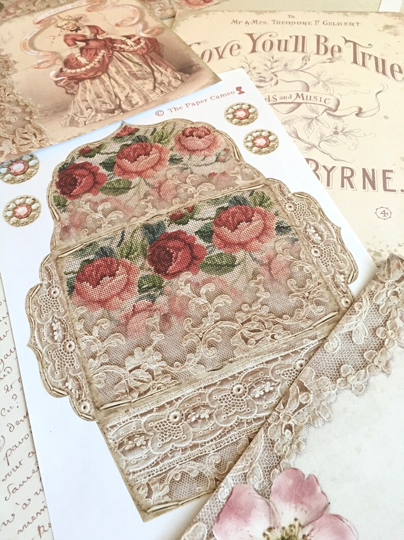 May include: A vintage-style card with a delicate lace design and embroidered floral motifs in shades of pink and green. The card features the text "Love You'll Be True" and "The Paper Cameo".