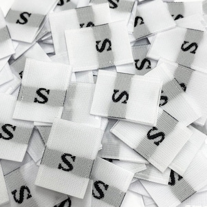 May include: A pile of white fabric labels with a black "S" printed on each. The labels are stacked and overlapping.
