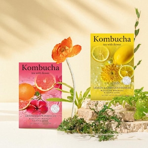 May include: Two boxes of Kombucha tea with flower. The box on the left is pink and features a grapefruit and hibiscus design. The box on the right is yellow and features a lemon and chrysanthemum design. Both boxes have the text "Kombucha tea with flower" and "KKOKDAM" on them.