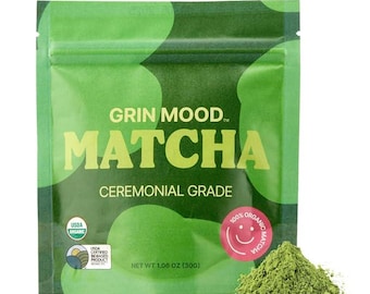 May include: A green pouch with the text "GRIN MOOD™ MATCHA CEREMONIAL GRADE" and a green and white USDA Organic Certified seal. The pouch contains 1.06 oz (30g) of green matcha powder. A small pile of green matcha powder is in the foreground.