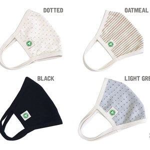 May include: Four different fabric face masks with a white border. The masks are in the colours black, light grey, oatmeal, and white with a dotted pattern. Each mask has a green logo with a leaf and the text "Organic 100" and "Global Organic Textile Standard GOTS".