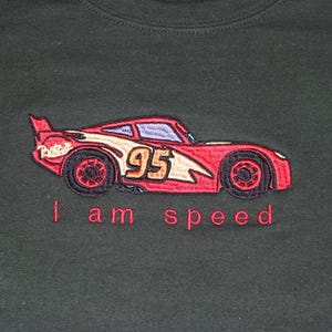 May include: Red and black embroidered design of a race car with the number 95 on the side. The text "i am speed" is below the car.