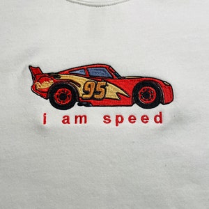 May include: White sweatshirt with a red, yellow, and black embroidered cartoon race car with the number 95 on the side. The text "i am speed" is embroidered below the car.
