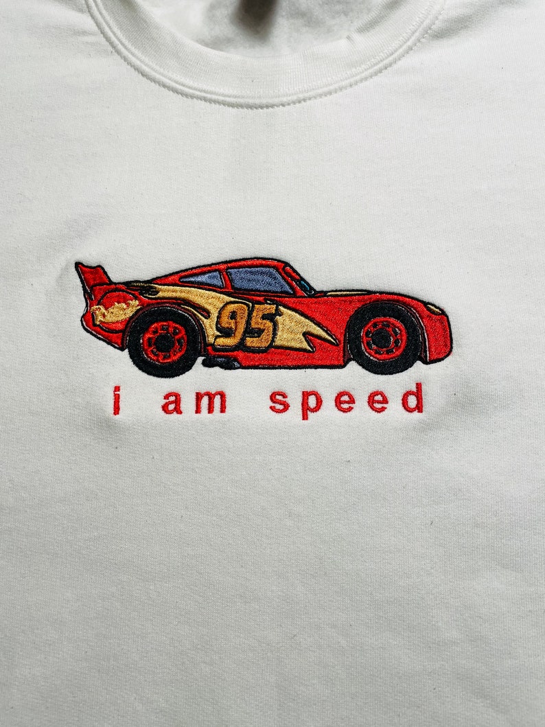 May include: White sweatshirt with a red, yellow, and black embroidered cartoon race car with the number 95 on the side. The text "i am speed" is embroidered below the car.