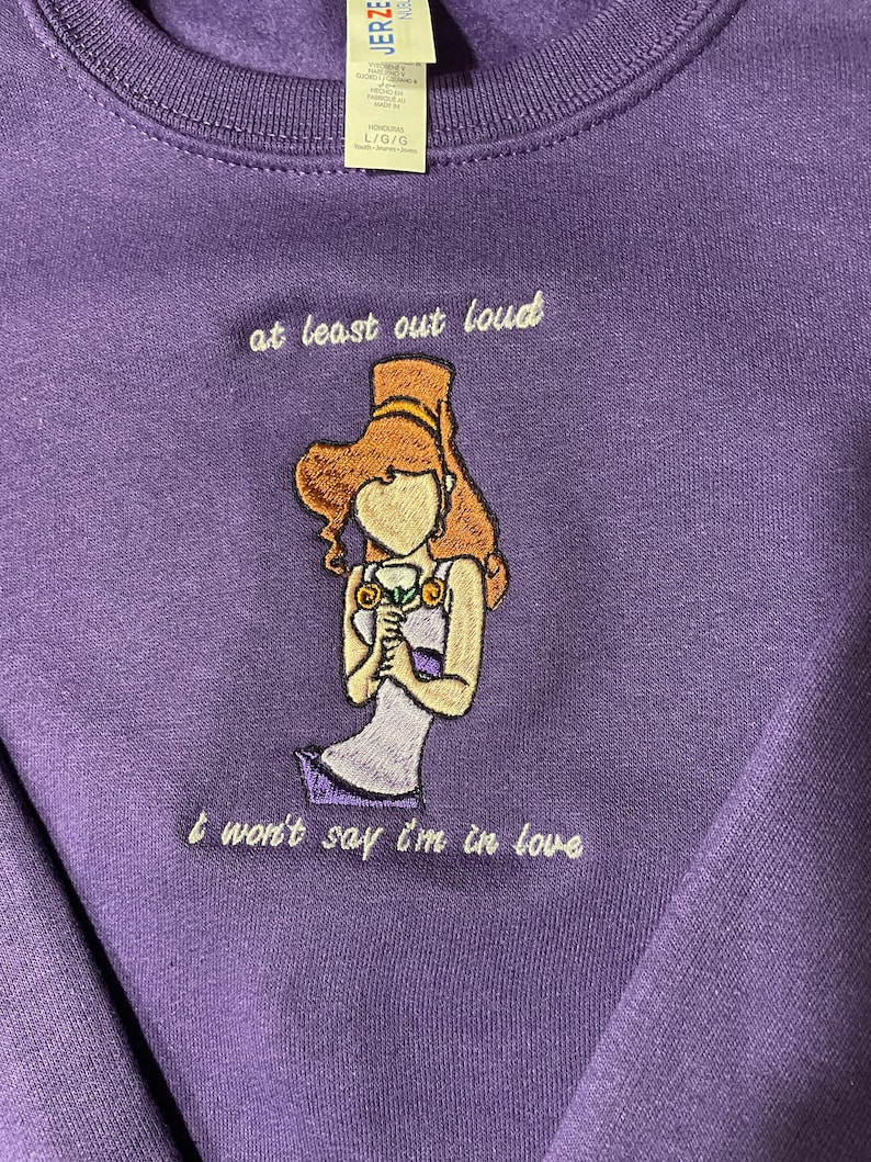 May include: Purple sweatshirt with an embroidered image of a woman holding a flower and the text "at least out loud I won't say I'm in love".