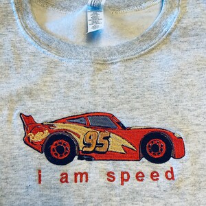 May include: A gray sweatshirt with a red and yellow embroidered image of a race car with the number 95 on the side. The text "i am speed" is embroidered below the car.