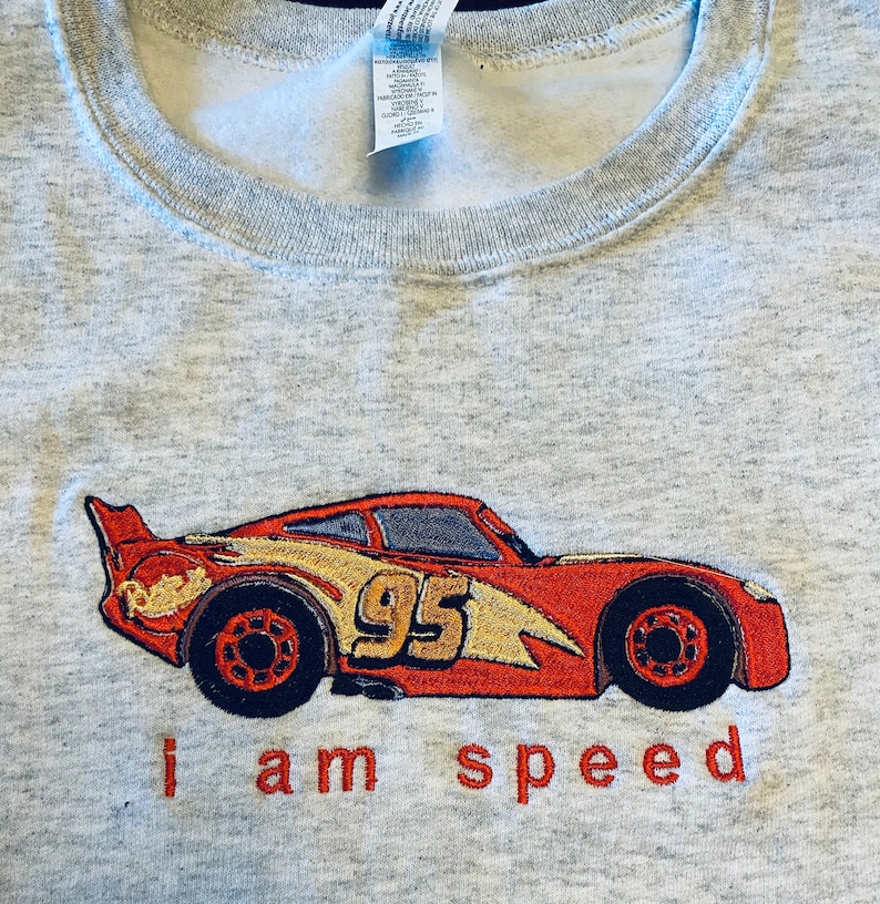 May include: A gray sweatshirt with a red and yellow embroidered image of a race car with the number 95 on the side. The text "i am speed" is embroidered below the car.