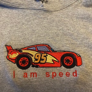 May include: Gray hooded sweatshirt with an embroidered image of a red race car with the number 95 on the side. The text "I am speed" is embroidered below the car.