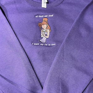 May include: Purple sweatshirt with an embroidered image of a woman with a crown and the text "at least out loud I won't say I'm in love"