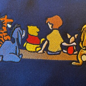 May include: Embroidered Winnie the Pooh and friends design on a navy blue sweatshirt. The characters include Winnie the Pooh, Piglet, Eeyore, Tigger, and Christopher Robin.