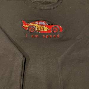 May include: Black sweatshirt with an embroidered image of a red race car with the number 95 on the side. The text "I am speed" is embroidered below the car.