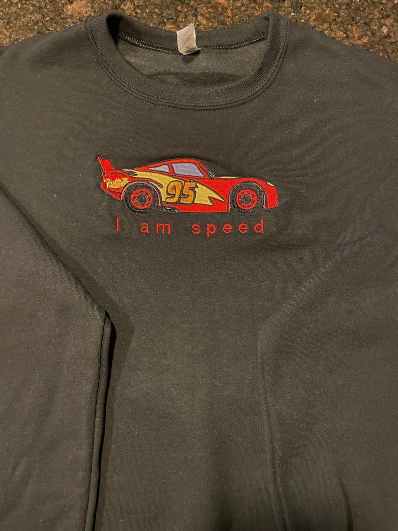 May include: Black sweatshirt with an embroidered image of a red race car with the number 95 on the side. The text "I am speed" is embroidered below the car.