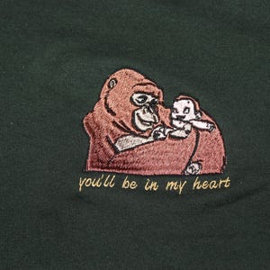 Puede incluir: Una camiseta verde con una imagen bordada de un orangut&aacute;n sosteniendo a un orangut&aacute;n m&aacute;s peque&ntilde;o. El texto "you'll be in my heart" est&aacute; bordado debajo de la imagen.