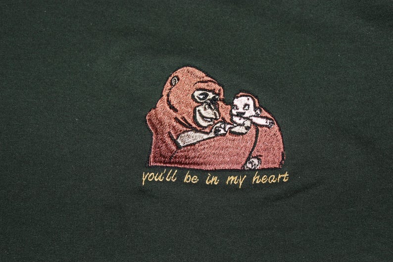 Puede incluir: Una camiseta verde con una imagen bordada de un orangut&aacute;n sosteniendo a un orangut&aacute;n m&aacute;s peque&ntilde;o. El texto "you'll be in my heart" est&aacute; bordado debajo de la imagen.