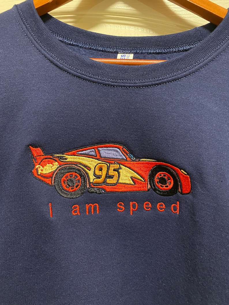 May include: A navy blue sweatshirt with an embroidered image of a red race car with the number 95 on the side. The text "I am speed" is embroidered below the car.