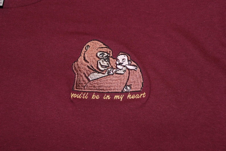 Puede incluir: Una camiseta de color granate con una imagen bordada de un orangut&aacute;n sosteniendo a un beb&eacute; orangut&aacute;n. El texto "you'll be in my heart" est&aacute; bordado debajo de la imagen.