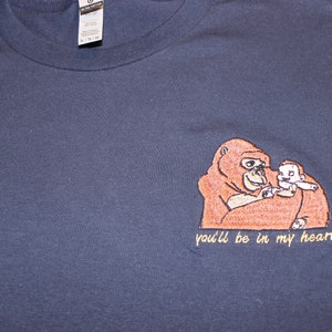 Puede incluir: Una camiseta azul marino con una imagen bordada de un orangut&aacute;n sosteniendo a un orangut&aacute;n m&aacute;s peque&ntilde;o. El texto "you'll be in my heart" est&aacute; bordado debajo de la imagen.