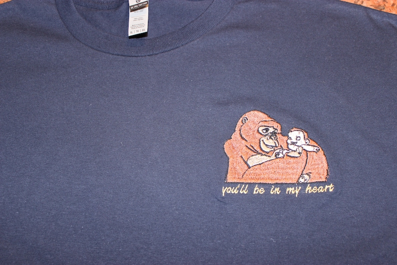 Puede incluir: Una camiseta azul marino con una imagen bordada de un orangut&aacute;n sosteniendo a un orangut&aacute;n m&aacute;s peque&ntilde;o. El texto "you'll be in my heart" est&aacute; bordado debajo de la imagen.