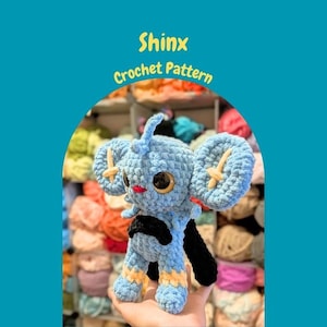 Peut inclure: Peluche Shinx bleue au crochet, avec de grandes oreilles et une queue noire. La peluche présente des accents jaunes et noirs sur les pattes et les oreilles. Le texte "Shinx Crochet Pattern" est affiché en jaune.