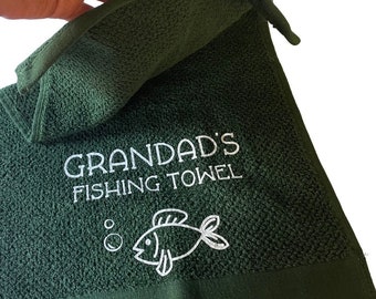 May include: A dark green hand towel with a white embroidered design of a fish and bubbles. The text "Grandad's Fishing Towel" is embroidered in white on the towel.