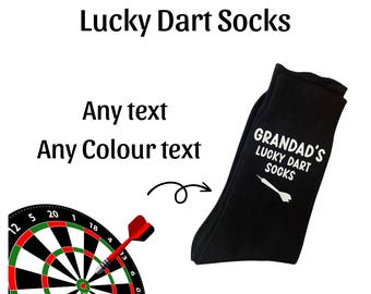 May include: Black socks with white text that reads "GRANDAD'S LUCKY DART SOCKS" and a white dart graphic. The socks are shown next to a dartboard.