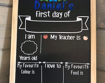 May include: A black chalkboard with a wooden frame, decorated with blue, green, and white bunting. The chalkboard has the text "Daniel's First day of" written in white. There are spaces for the child's age, favorite color, favorite food, and what they want to be when they grow up.