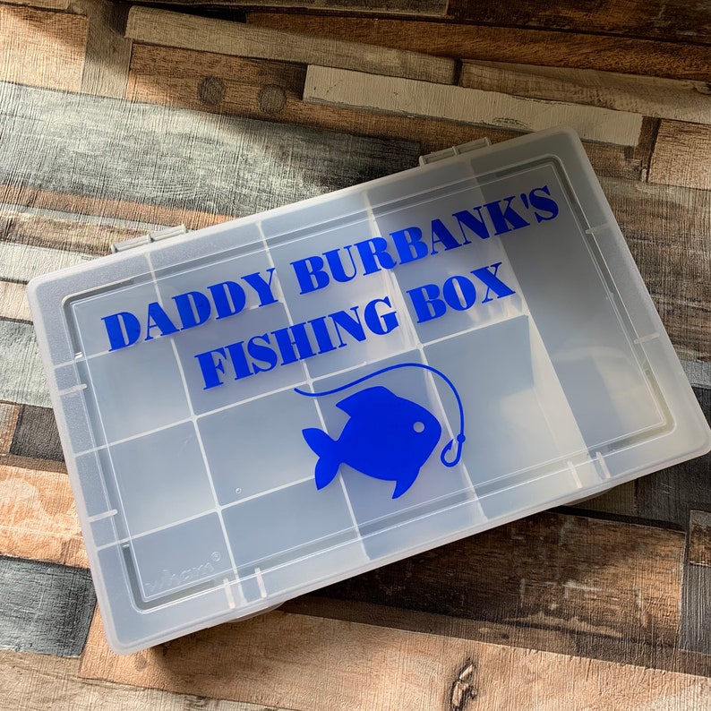 May include: A clear plastic fishing tackle box with a blue graphic of a fish and the text "Daddy Burbank's Fishing Box".