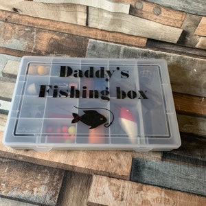 May include: A clear plastic tackle box with multiple compartments. The box is filled with fishing lures and other fishing gear. The lid of the box has a black vinyl sticker that says "Daddy's Fishing Box".