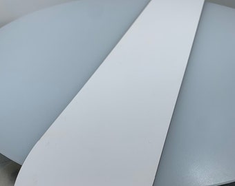 May include: A white, elongated, teardrop-shaped object with a rounded end and a straight edge. The object is positioned on a light gray surface, creating a contrast between the two elements. The object appears to be made of a smooth, solid material.