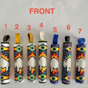 Könnte beinhalten: Sieben zylindrische, mit Perlen besetzte Objekte mit Leder- oder Stoffschlaufen. Jedes hat einen weißen Hintergrund mit einem farbenfrohen geometrischen Design und einer Büffelsilhouette. Der Text "FRONT" steht oben. Die Schlaufen sind schwarz, gelb, braun, weiß, blau, schwarz und blau.