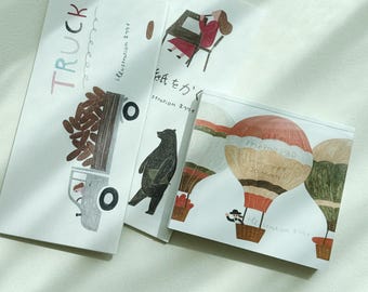 Puede incluir: Tres tarjetas ilustradas con diferentes diseños. La primera tarjeta presenta un camión con una cama llena de troncos. La segunda tarjeta presenta un oso y un globo aerostático. La tercera tarjeta presenta un globo aerostático con el texto "Trema 1240" en él.