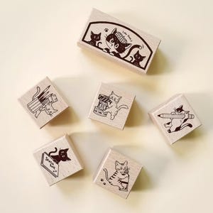 May include: A set of wooden stamps with black and white cat illustrations. The stamps show cats with pencils, cameras, and sketchbooks. One stamp has the text "My Desk". The stamps are ideal for crafting and scrapbooking.