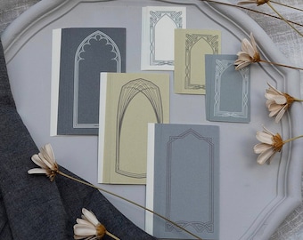 Puede incluir: Seis marcos de papel decorativos con un diseño arqueado. Los marcos son en tonos grises y beige. Los marcos están sobre una superficie blanca.