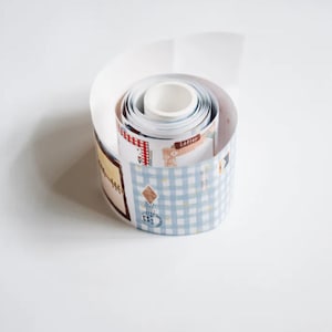 May include: A roll of adhesive paper tape featuring a repeating pattern of light blue gingham, vintage-style postage stamps, and decorative frames. The tape is coiled into a cylinder, displaying various printed designs including the word Letter.