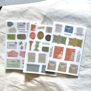 Puede incluir: Tres hojas de pegatinas de estilo vintage con varios diseños. Las pegatinas presentan sellos postales, sobres y elementos decorativos en colores pastel. El texto incluye "Vintage Joy" y "Little Joy."