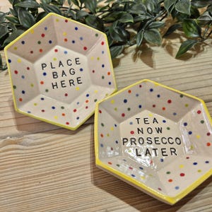 Puede incluir: Dos platos hexagonales de cer&aacute;mica con bordes amarillos y lunares de colores. Un plato dice "Place Bag Here" y el otro dice "Tea Now Prosecco Later".
