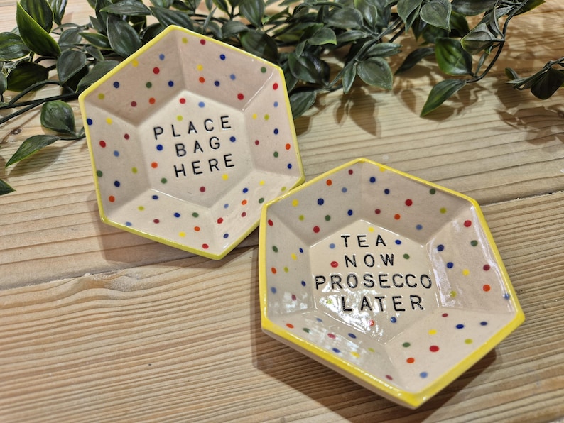 Puede incluir: Dos platos hexagonales de cer&aacute;mica con bordes amarillos y lunares de colores. Un plato dice "Place Bag Here" y el otro dice "Tea Now Prosecco Later".