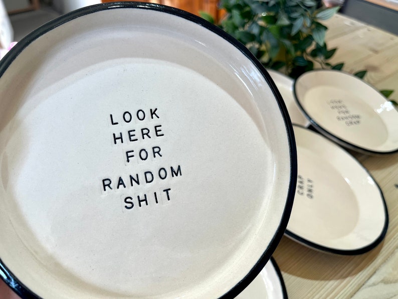 Może przedstawiać: Biała ceramiczna miska z czarnym rantem. Miska ma nadrukowany tekst "LOOK HERE FOR RANDOM SHIT".