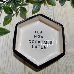 Puede incluir: Un plato hexagonal de cer&aacute;mica blanca con un borde negro. El plato tiene el texto "TEA NOW COCKTAILS LATER" escrito en negro.