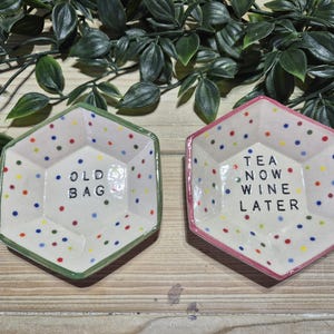 Puede incluir: Dos platos hexagonales de cer&aacute;mica con lunares coloridos. Un plato es verde y dice "Old Bag" y el otro es rosa y dice "Tea Now Wine Later".