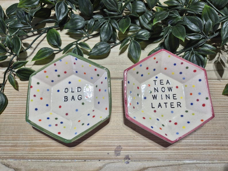 Puede incluir: Dos platos hexagonales de cer&aacute;mica con lunares coloridos. Un plato es verde y dice "Old Bag" y el otro es rosa y dice "Tea Now Wine Later".
