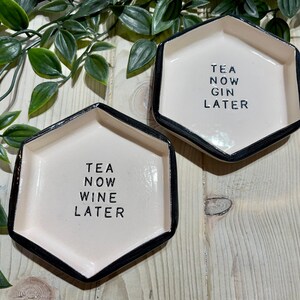 Puede incluir: Dos platos hexagonales de cer&aacute;mica blanca con borde negro. Un plato dice "TEA NOW WINE LATER" y el otro dice "TEA NOW GIN LATER".