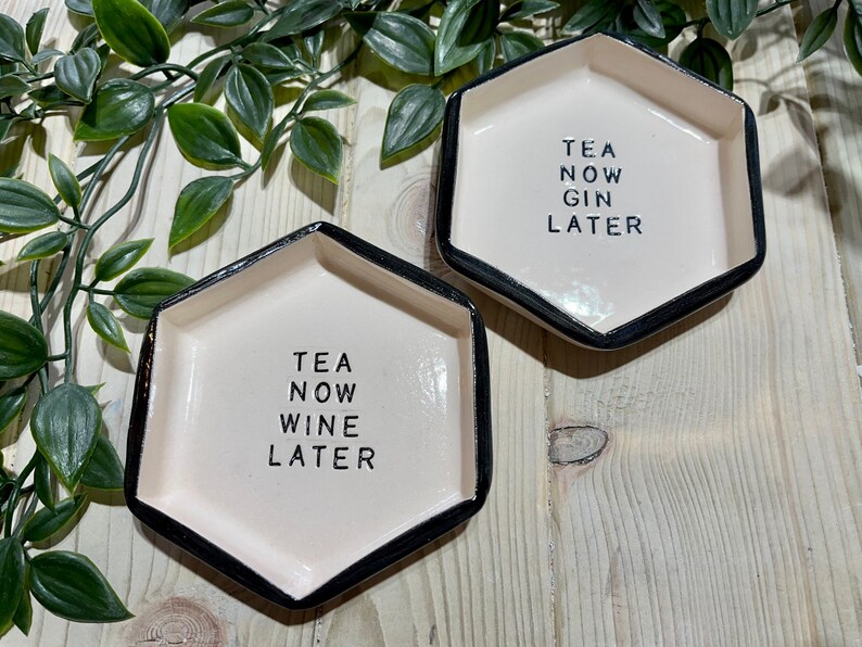Puede incluir: Dos platos hexagonales de cer&aacute;mica blanca con borde negro. Un plato dice "TEA NOW WINE LATER" y el otro dice "TEA NOW GIN LATER".
