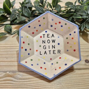 Puede incluir: Un plato hexagonal de cer&aacute;mica con un borde azul y un fondo blanco. El plato est&aacute; decorado con lunares de colores y el texto "TEA NOW GIN LATER".